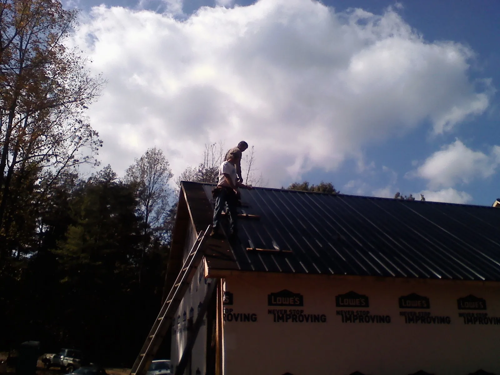 Roofer fastening dark metal panels high against a cloudy sky, from a Roof Inspection job in Carson